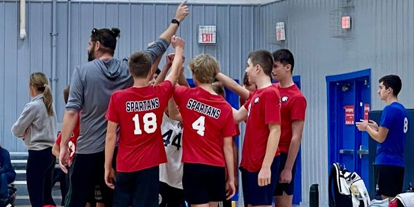Youth basketball team Spartans huddle during a timeout in a gym.
