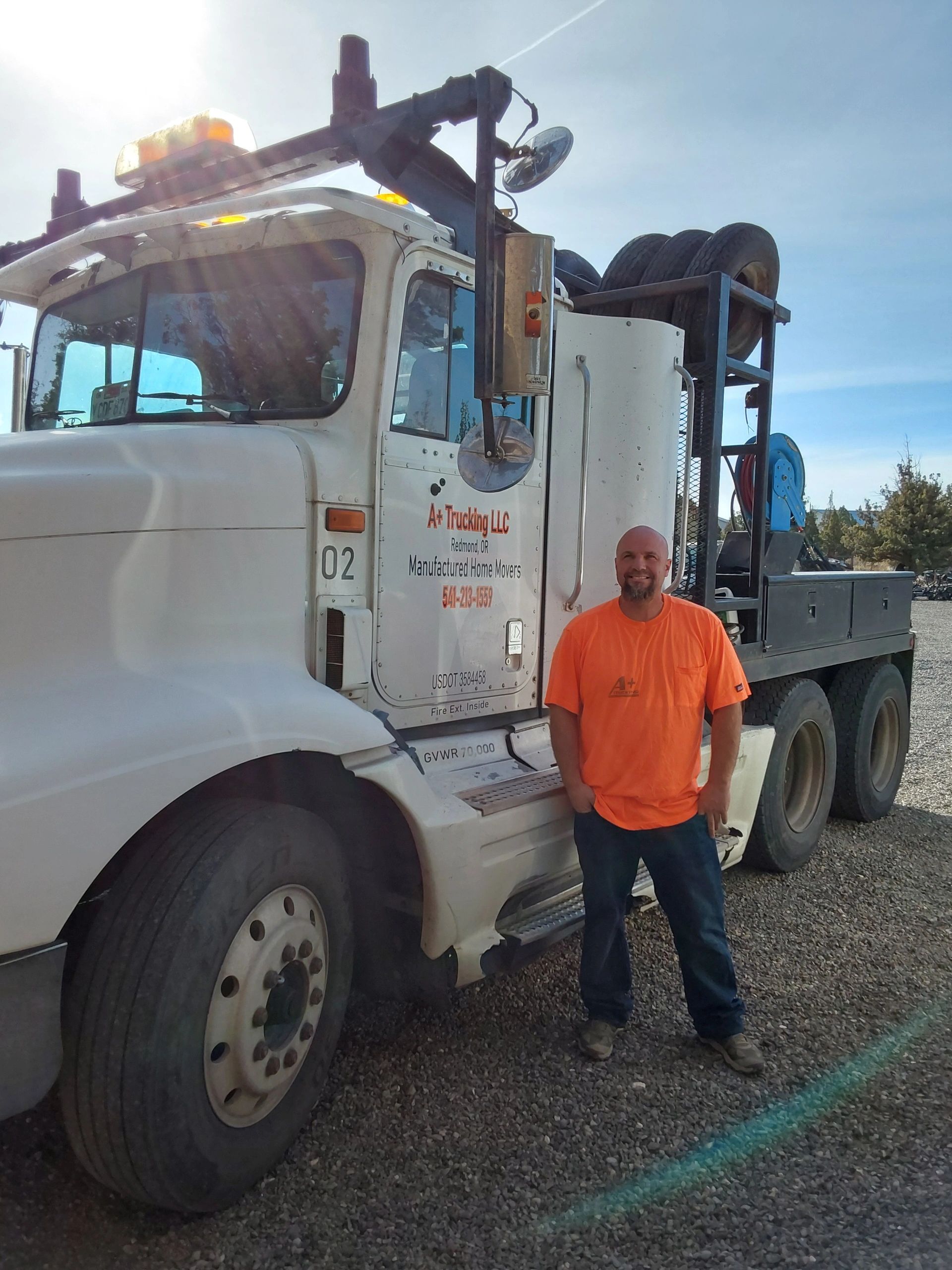 Man in orange shirt standing beside a white truck with company signage.