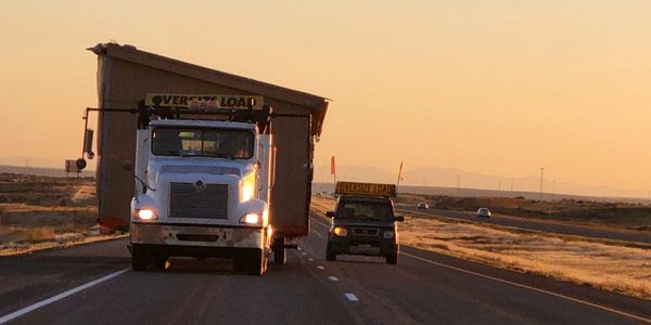 Truck and car carrying an oversized load on an empty highway at sunset.