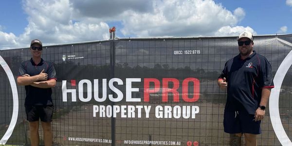 Two men stand by a House Pro Property Group banner outdoors under a cloudy sky.