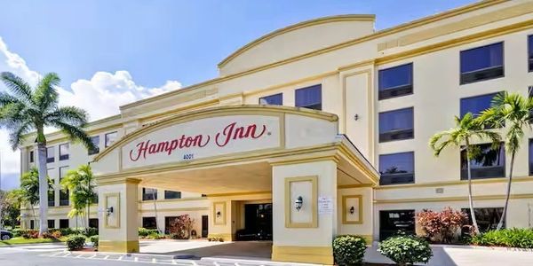 Exterior view of Hampton Inn hotel with clear sky and palm trees.