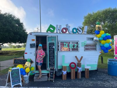 Colorful photo booth trailer with balloons and decorative letters outdoors.