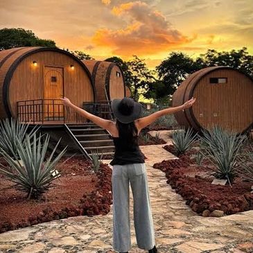 Mujer frente a cabañas redondas al atardecer.