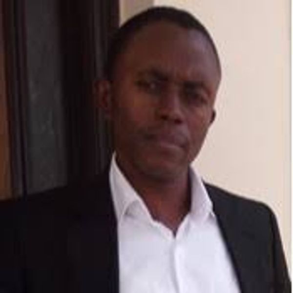 Man in a black suit and white shirt standing indoors.