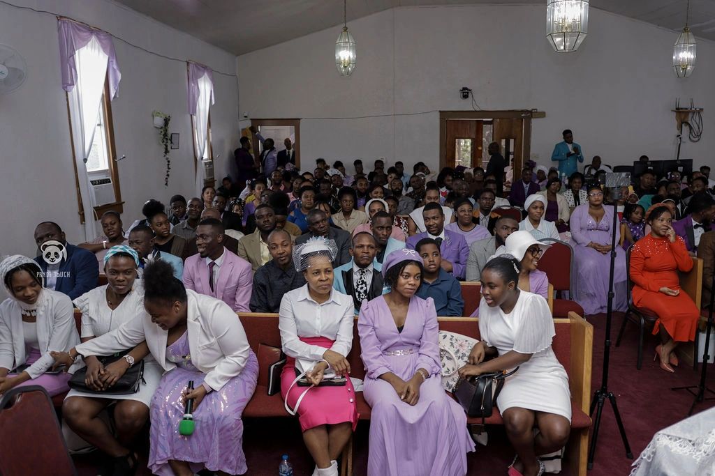 A large group of people attending a formal event in a hall, many dressed in purple and white.