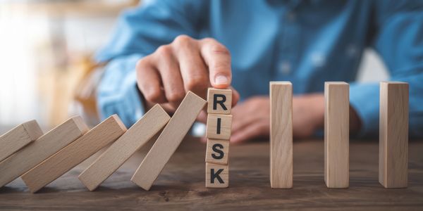 Hand stopping falling blocks with 'RISK' blocks.