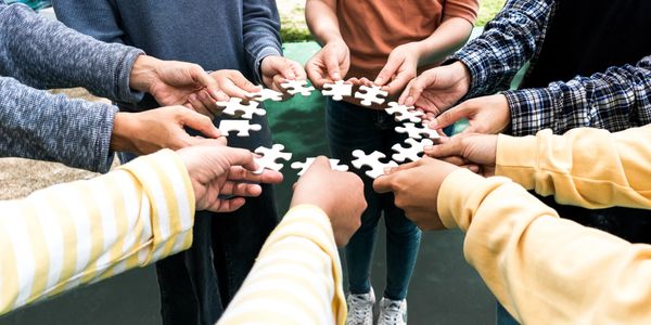 Group of people holding puzzle pieces together in a circle.