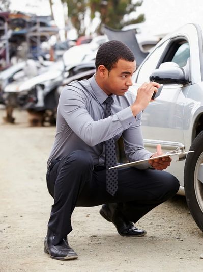 Man inspecting car damage and taking notes with clipboard.