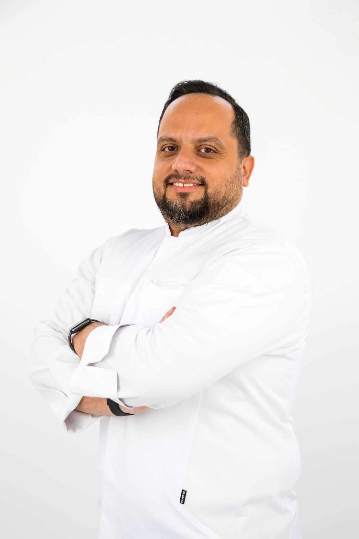 Smiling man in a white chef jacket with folded arms.