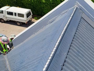Workers sealing a metal roof ridge with fresh sealant.