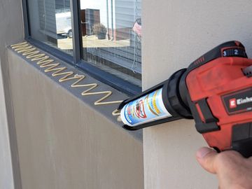 Applying sealant in a zigzag pattern along a window frame using a caulking gun.