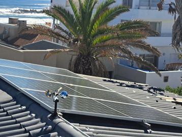 Solar panels on a rooftop with a palm tree and ocean view in the background.