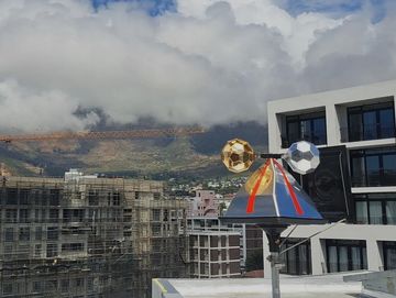 A reflective weather instrument on a rooftop with mountains and clouds in the background.