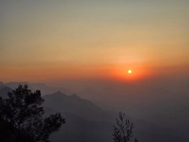 Sunset over misty mountains with silhouetted trees.