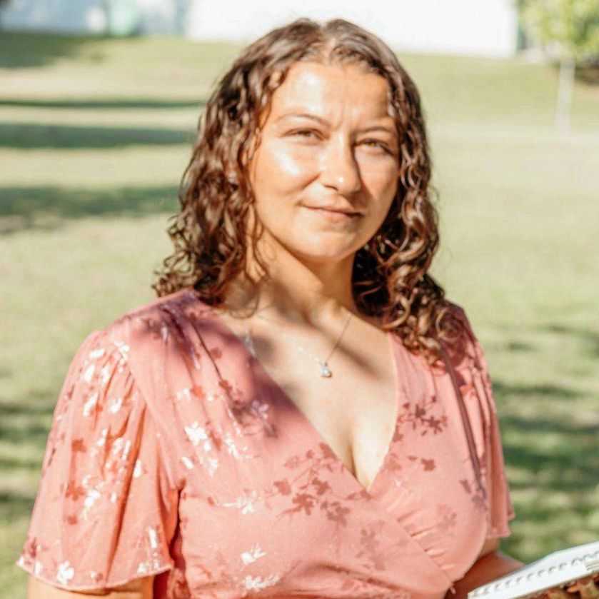 Woman in a pink floral dress holding a notebook outdoors.