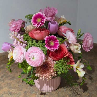 A vibrant bouquet of mixed pink flowers in a ribbed pink vase.