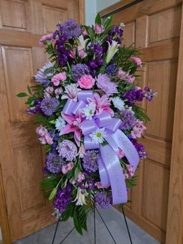 Tall floral arrangement with purple, pink, and white flowers and a lavender ribbon.