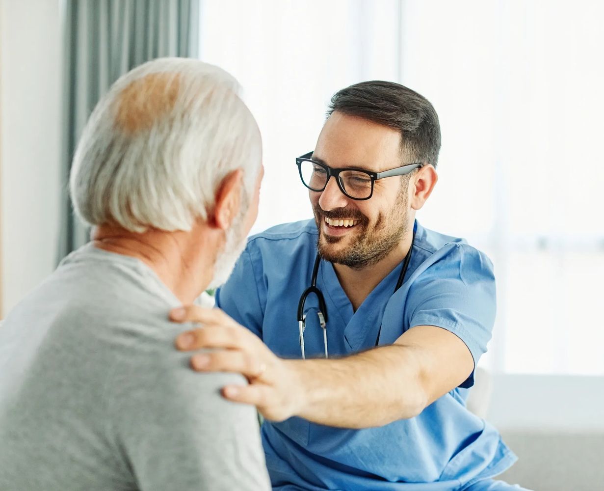 A smiling male nurse comforts an elderly man during a consultation.