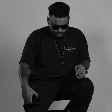 Man in sunglasses sitting on a stool with moody purple lighting.