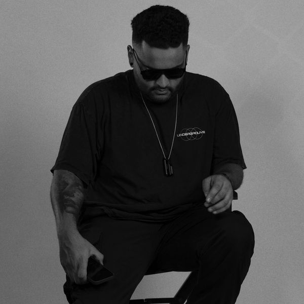 Man in sunglasses sitting on a stool with moody purple lighting.