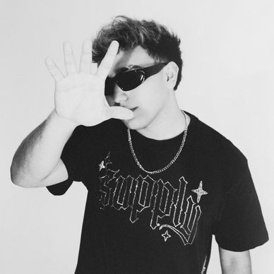Man in sunglasses with hand raised, wearing a black shirt and chain.