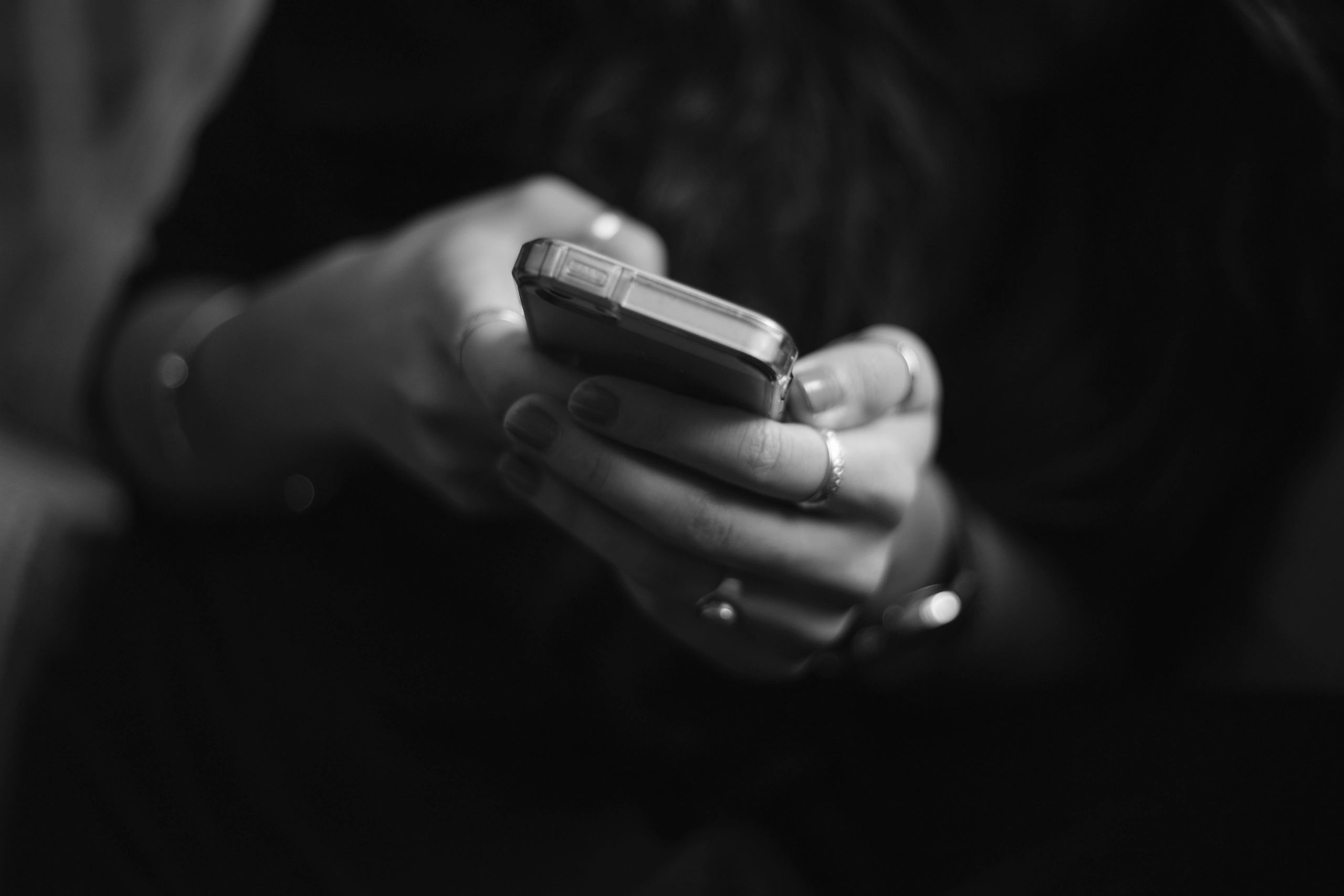 Close-up of hands holding a smartphone with multiple rings and muted nail polish.