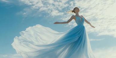 Woman in a flowing blue dress stands gracefully against a cloudy sky.
