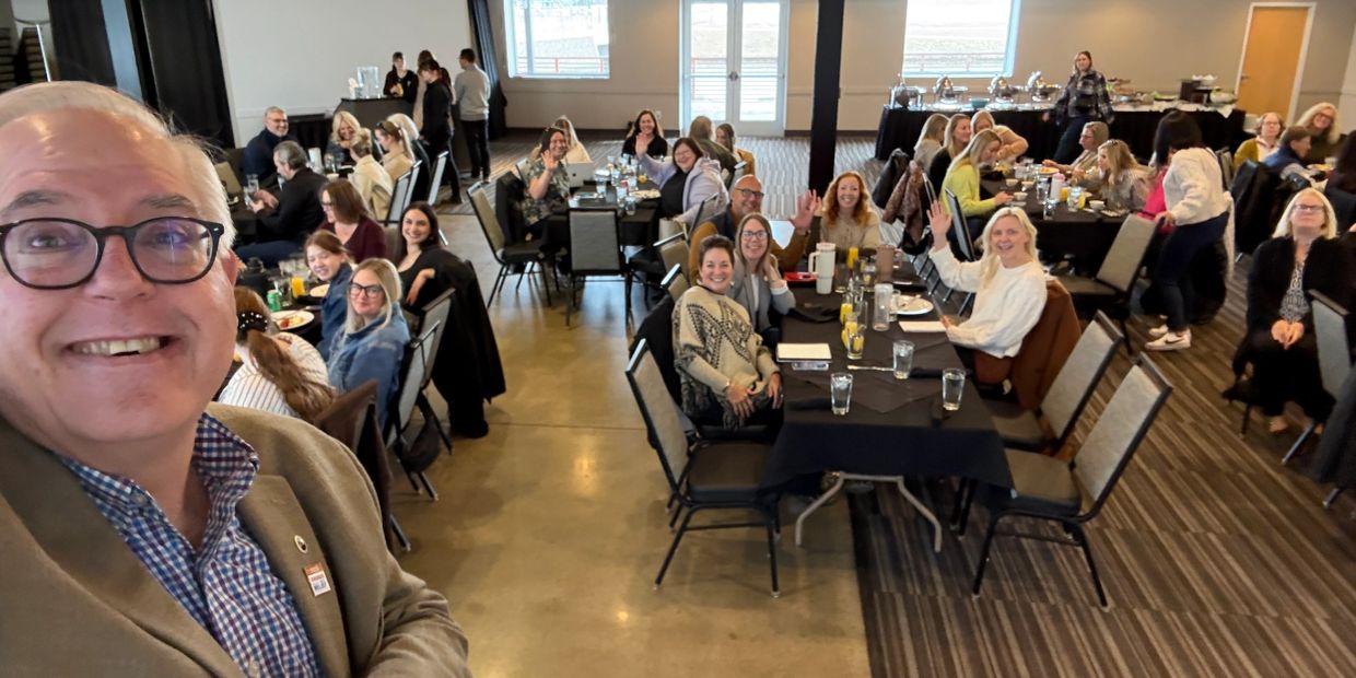 Group selfie with people waving at a dinner event.