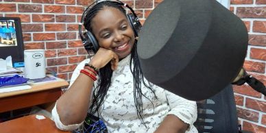 Woman with headphones smiling in a radio studio.