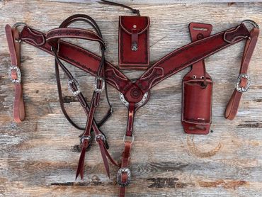 Intricately designed leather horse tack with silver buckles on a wooden surface.