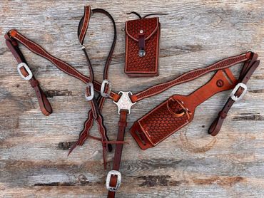 Intricately tooled leather equestrian tack with silver buckles on rustic wooden surface.