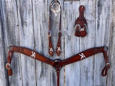 Brown leather horse tack with silver buckles hanging on a wooden fence.