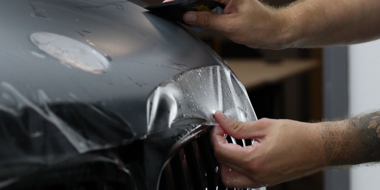 Applying a protective film on a car's hood by hand.