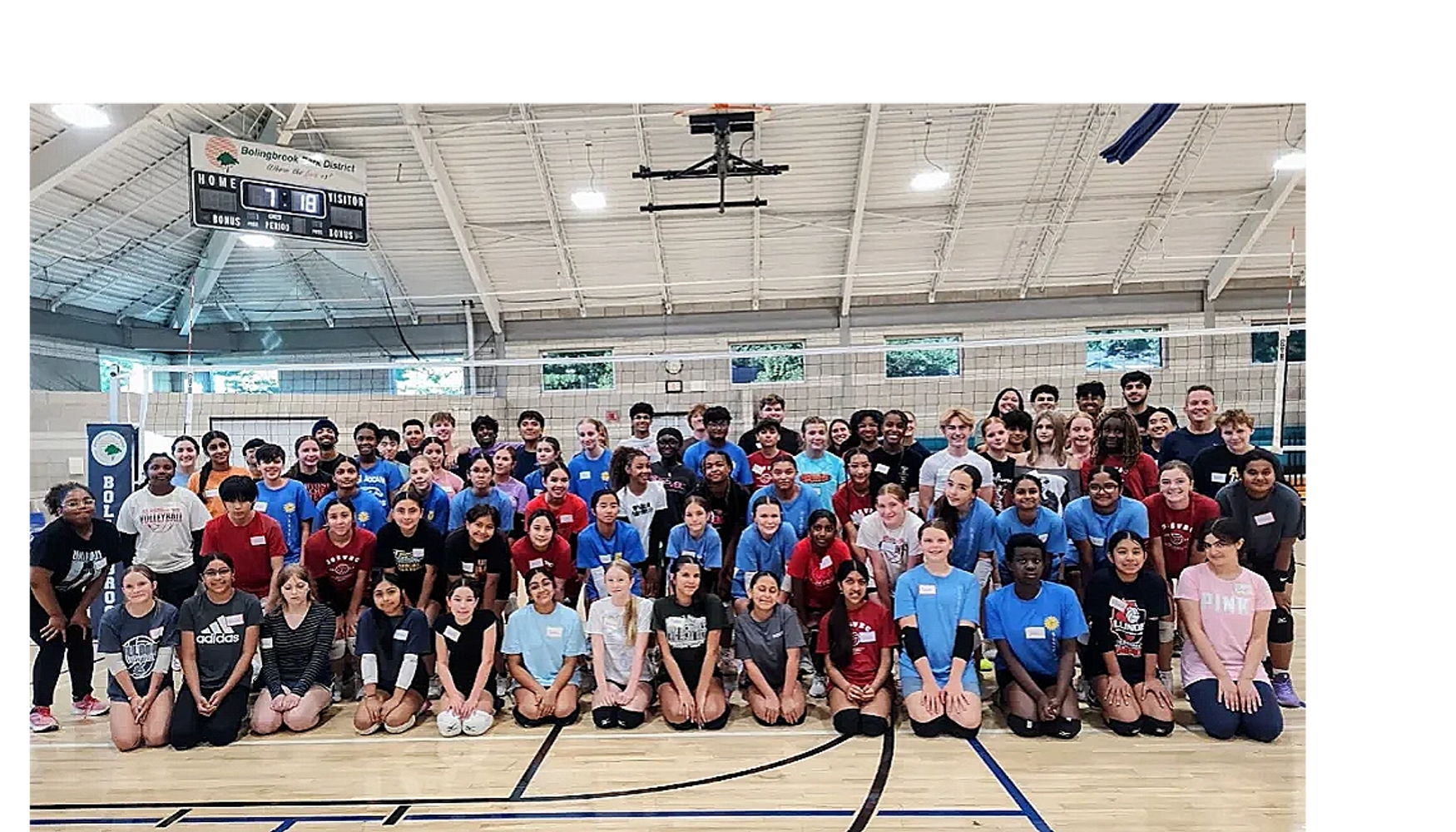 Large group of kids and teenagers posing in a gymnasium by a volleyball net.
