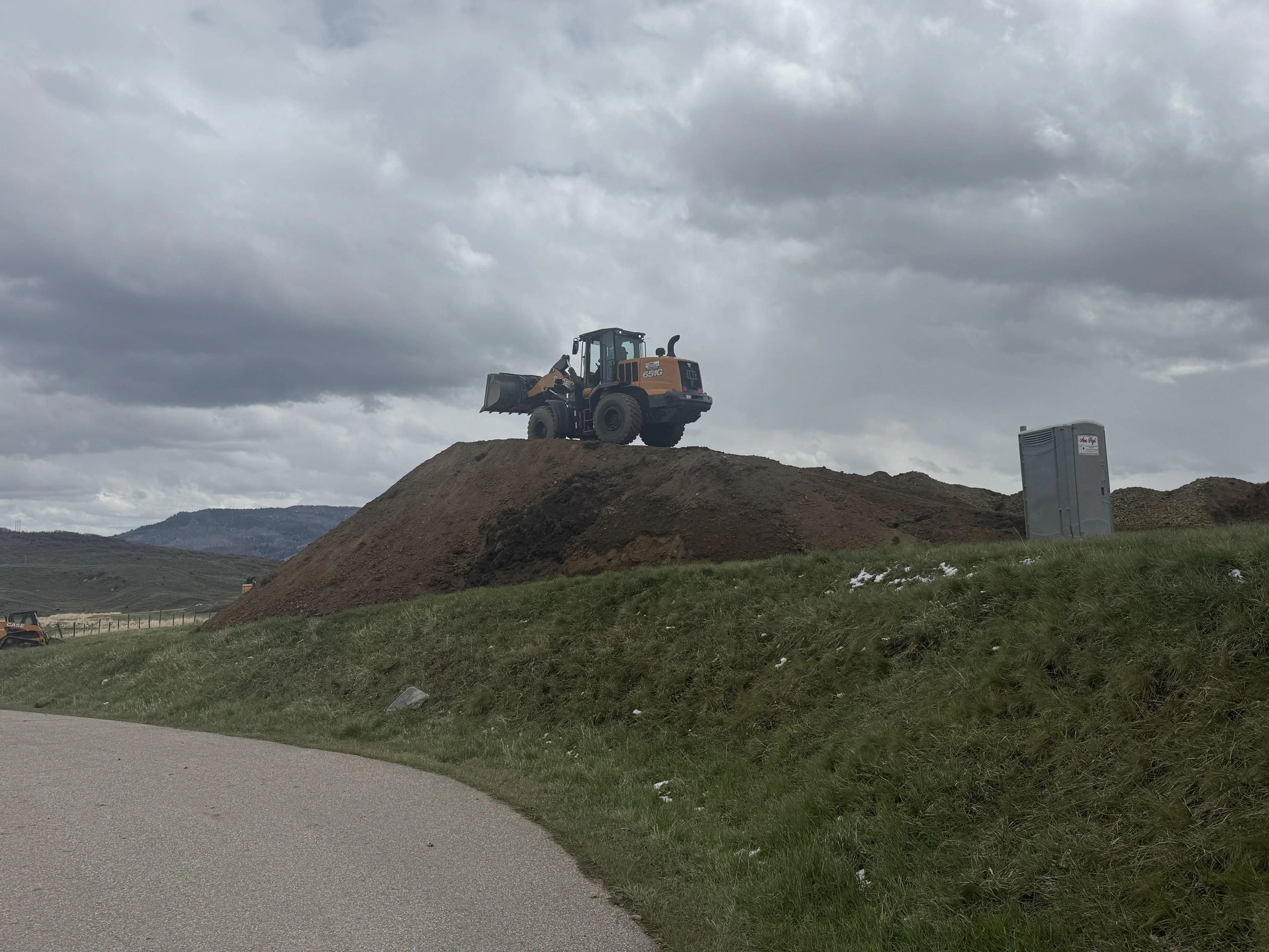 Construction loader on a dirt mound under cloudy sky.