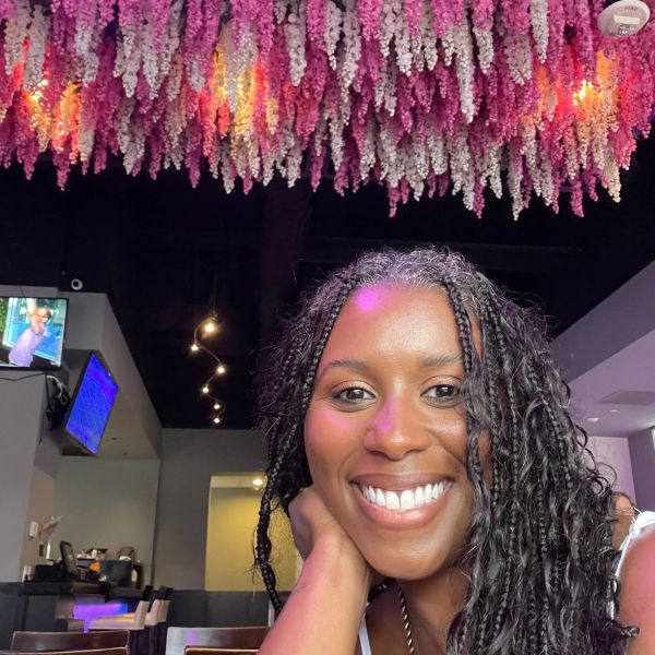 Smiling woman with braided hair under vibrant hanging flowers.