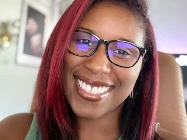 Smiling woman with glasses and red-tinted hair.