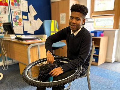 Student in uniform holding a bicycle wheel in classroom.