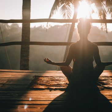 Person meditating in lotus pose at sunrise on a wooden deck.