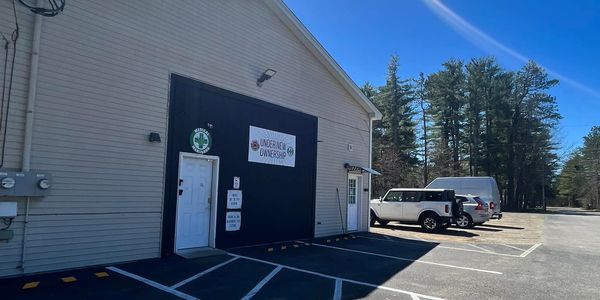 Exterior view of a commercial building with parking lot and vehicles under a clear blue sky.