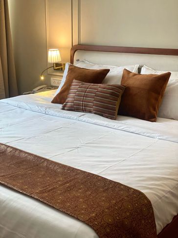 Cozy bed with white linens and brown decorative pillows under warm lighting.