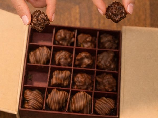 Box of assorted chocolates with two held pieces.