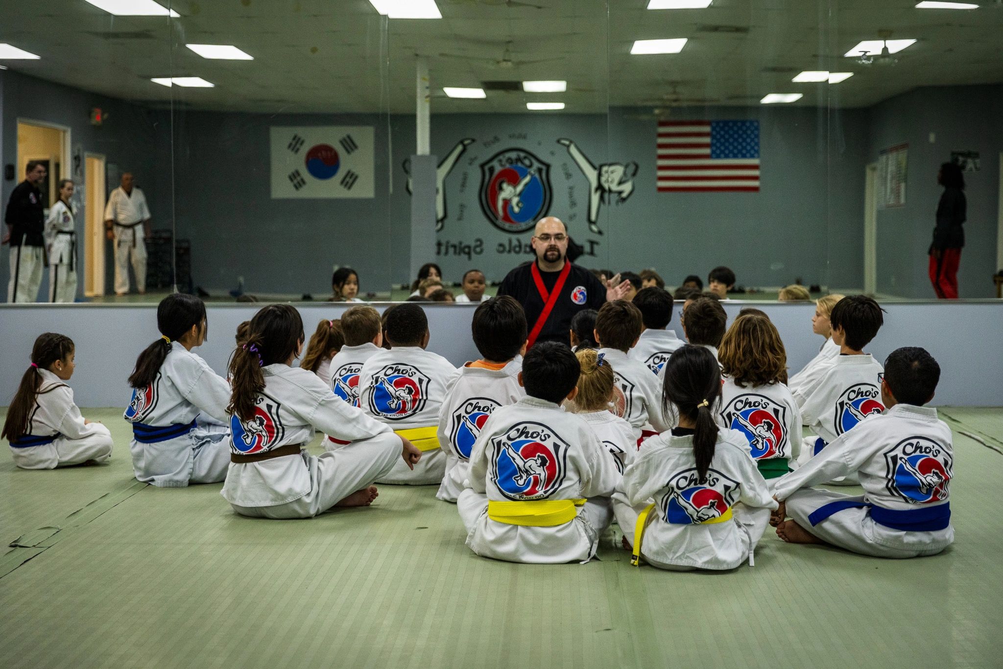 Martial arts instructor teaching a class of children in uniforms with flags on the wall.