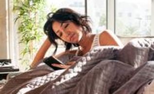 woman looking at her phone while resting on a mattress under a weighted blanket