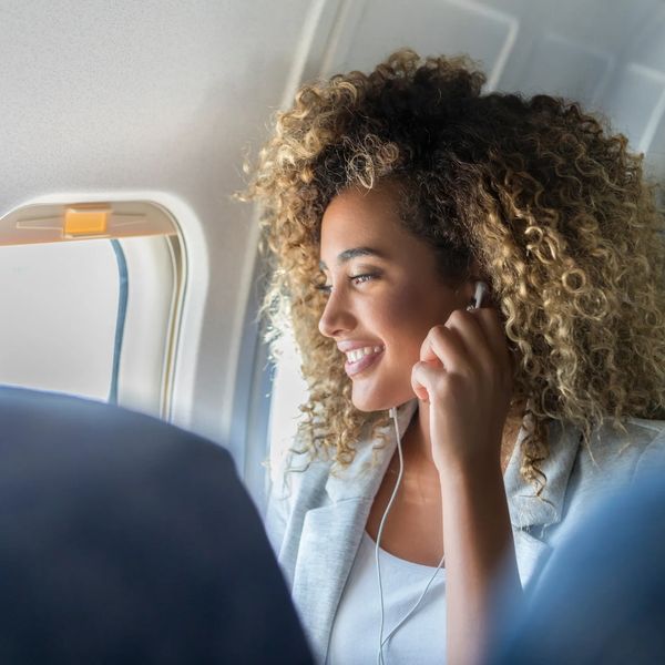 Woman on a plane, seated, holding her hand to an earphone in her ear.