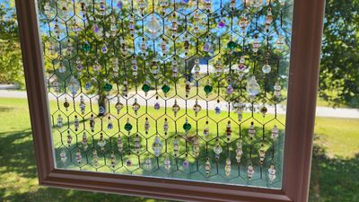Decorative hanging beads in a hexagonal frame catch sunlight by a window.