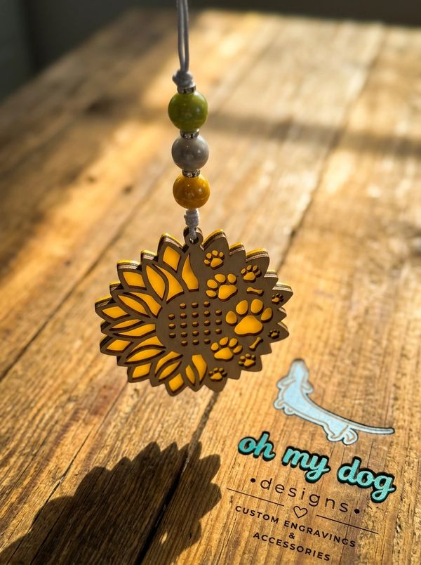Sunflower pendant with paw prints hanging against a wooden background.