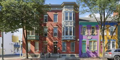 Colorful row houses with trees and parked cars.