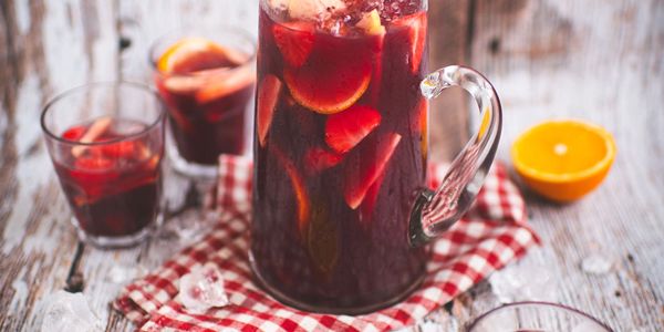 Jarra de sangría con frutas y vasos sobre una mesa.