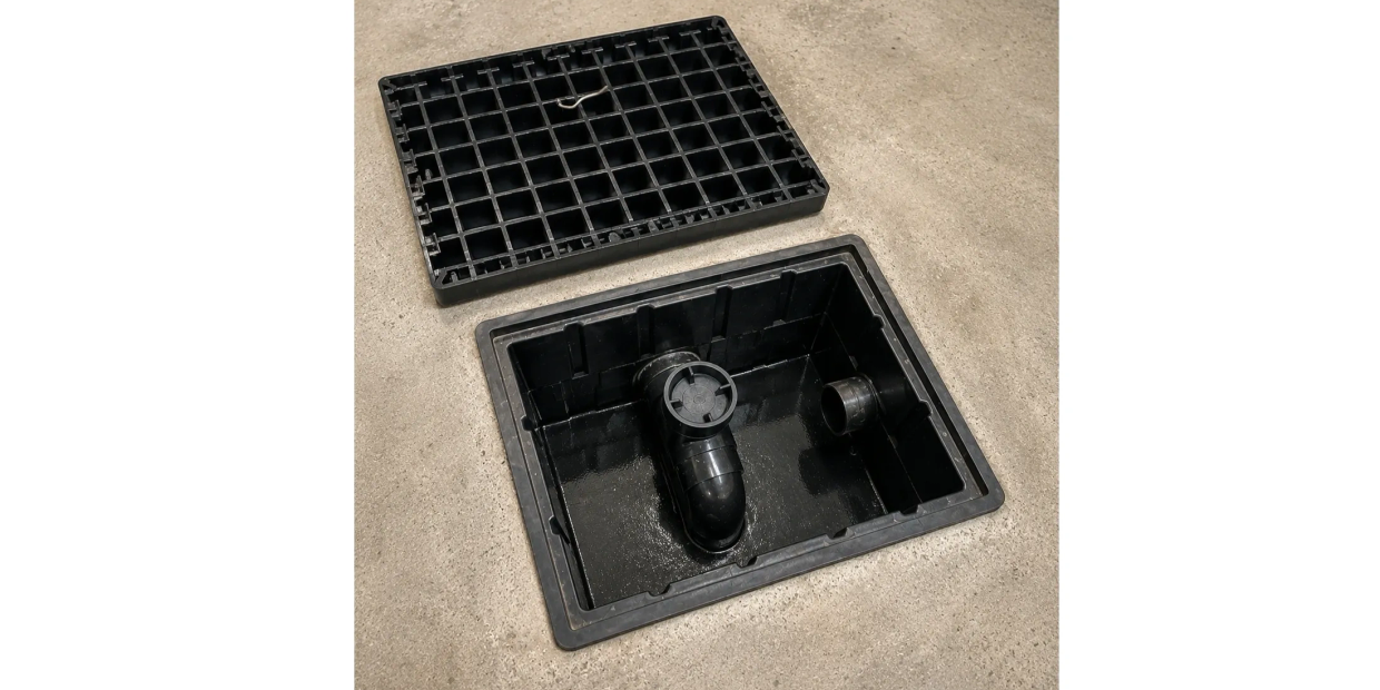 Boîte d'inspection en plastique noire avec couvercle retiré sur sol en béton.